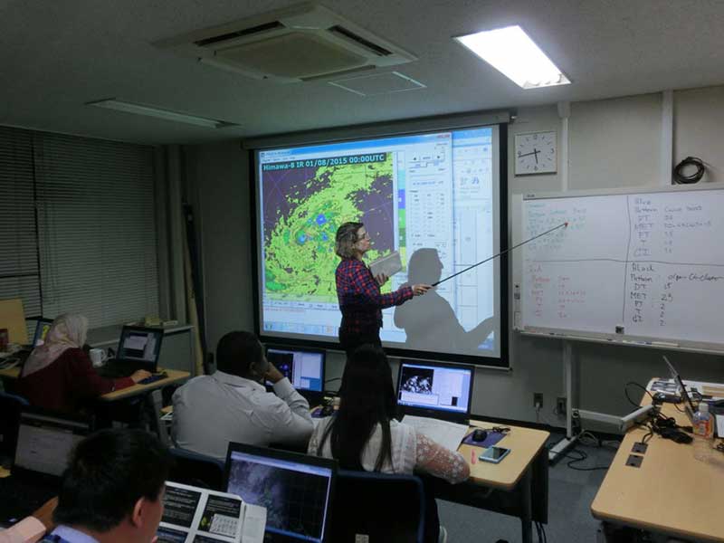 People listening to a woman pointing at a whiteboard using a telescopic pointer