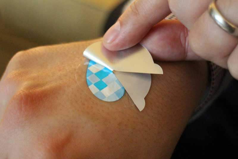 Close-up of human fingers peeling of the top layer of sensor patch applied to the hand