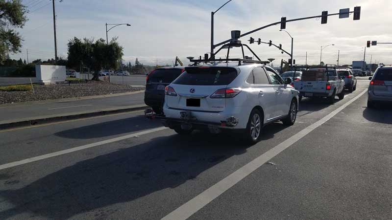 A white self-driving Lexus equipped with lidar tech waiting at an intersection
