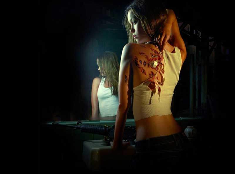 A humanoid female robot standing in front of a mirror with wounds revealing metal on her back