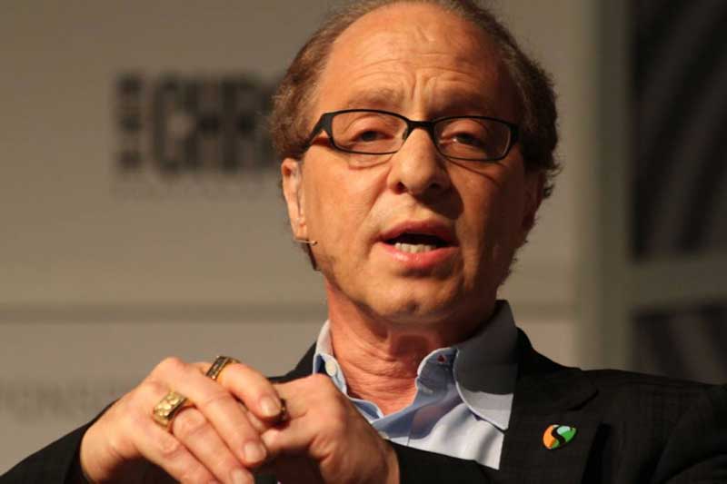 Ray Kurzweil sitting, wearing a microphone, and talking