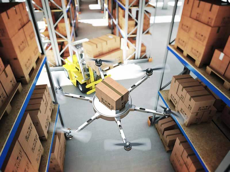 A drone carrying a package hovers inside a warehouse