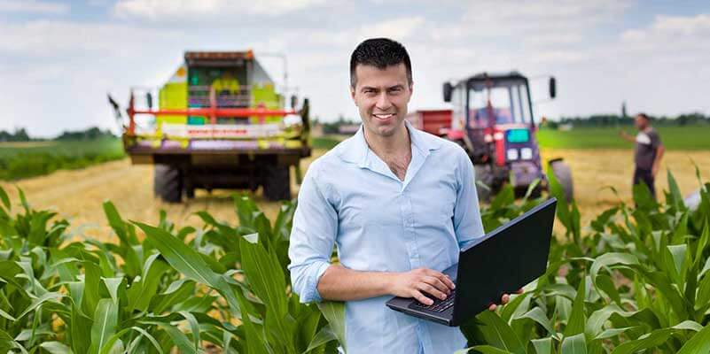 Man in cornfield with laptop and tractors