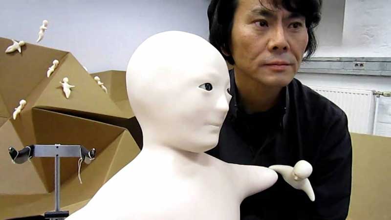A man holding a white humanoid robot, with several smaller white robots in the background