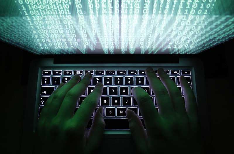 Two hands typing on the keyboard of a laptop with a screen showing binary code