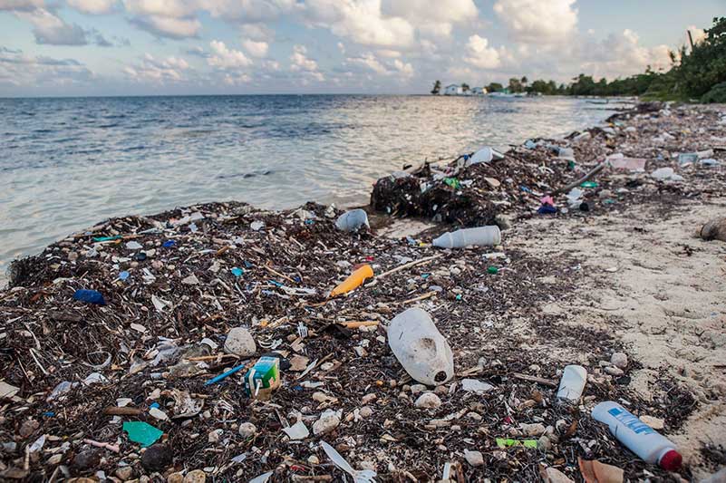 A garbage-filled beach with a sea and partly cloudy sky in the background