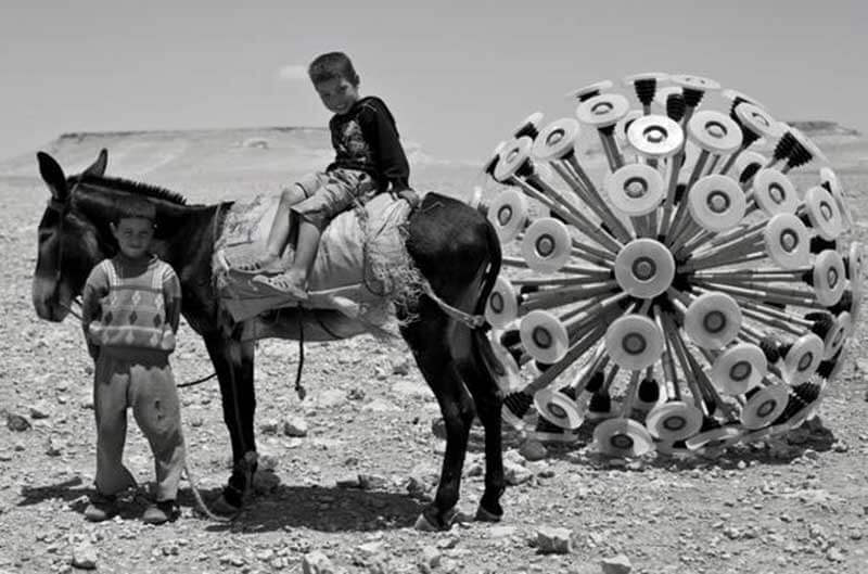 A boy sitting on a donkey and another boy standing next to him and the Mine Kafon ball behind them