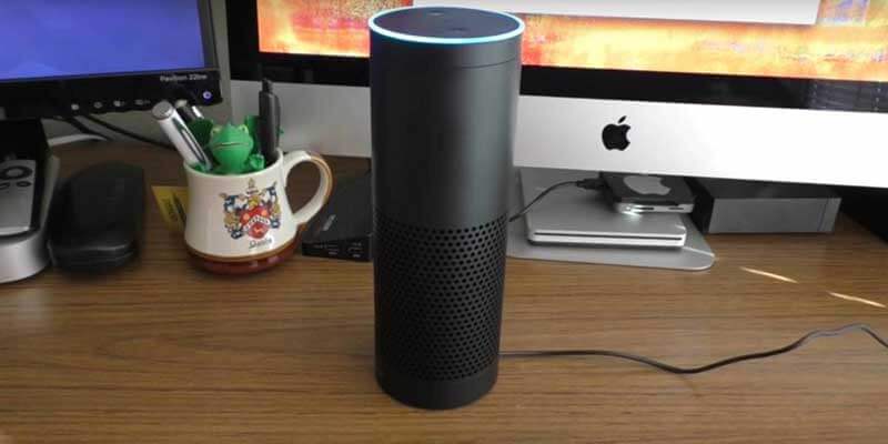 An Amazon Echo smart speaker on a work desk with two computer monitors behind it