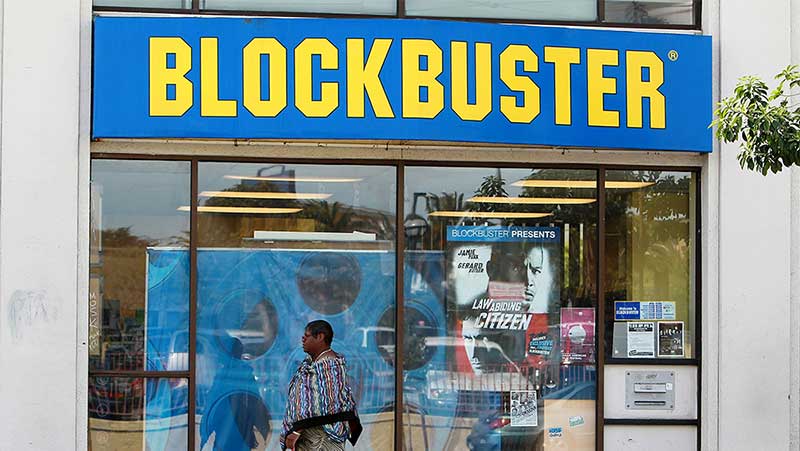 A person walking in front of a Blockbuster store with a poster for the movie “Law abiding citizen” on the storefront