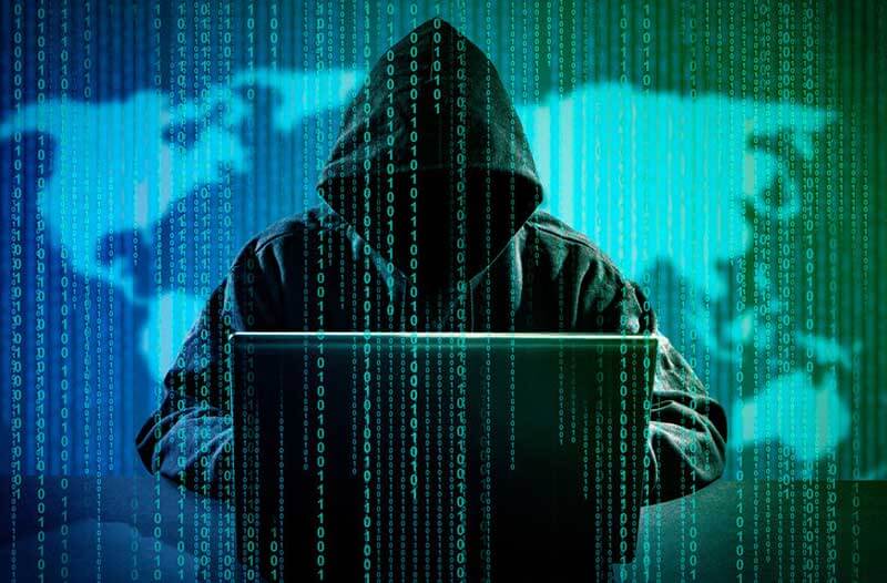 A hacker with a hoodie in front of a laptop against a green and blue background with the world map