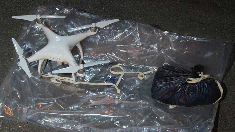 White drone connected with a strap to a black trash bag
