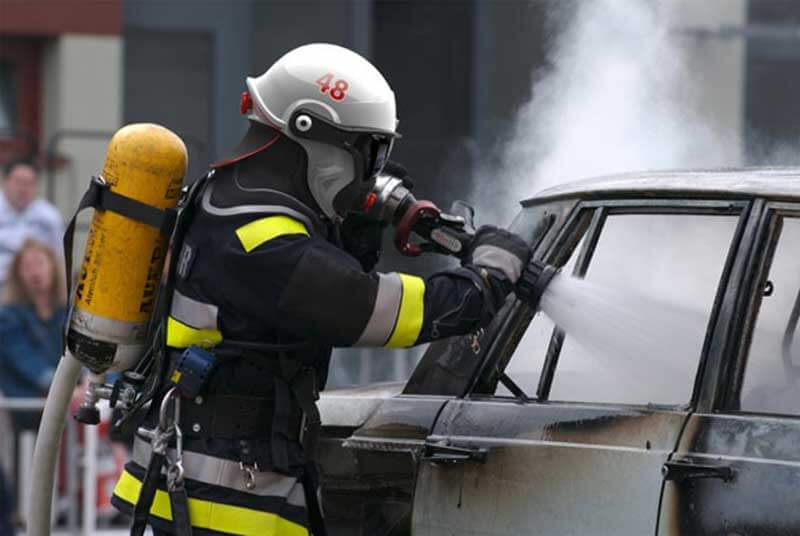 A firefighter putting out flames in a burning car