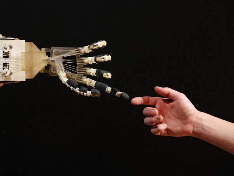 Robotic hand almost touching a human hand on a black background