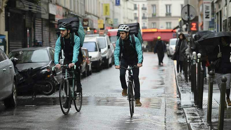 Two Deliveroo drivers riding bikes on a rainy day