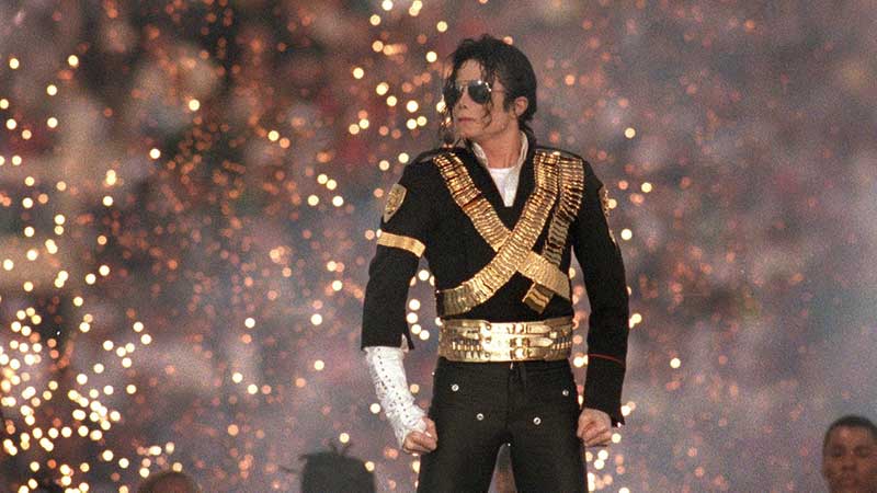 Michael Jackson standing on stage with sunglasses on and sparks flying in the background