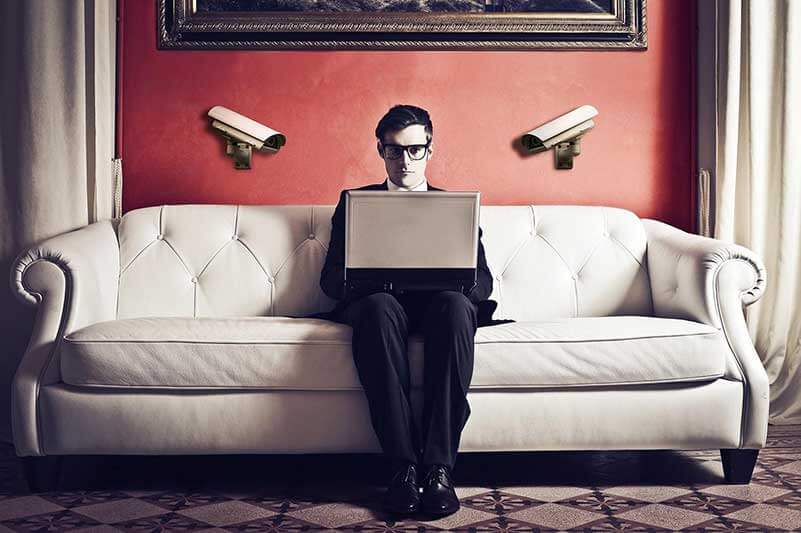 Man with spectacles sits on white couch with laptop