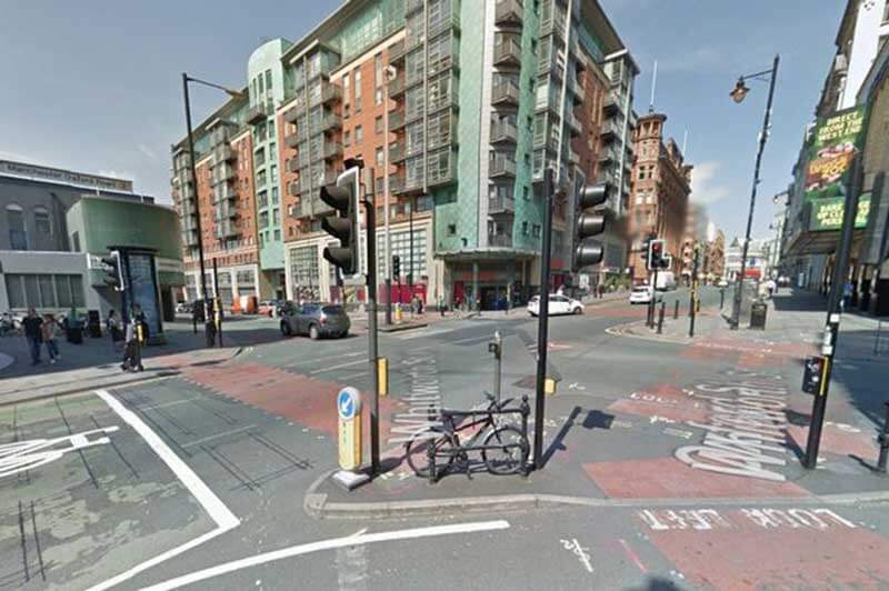 A crossroad in the city with pedestrian crossings and a small number of cars and people passing by