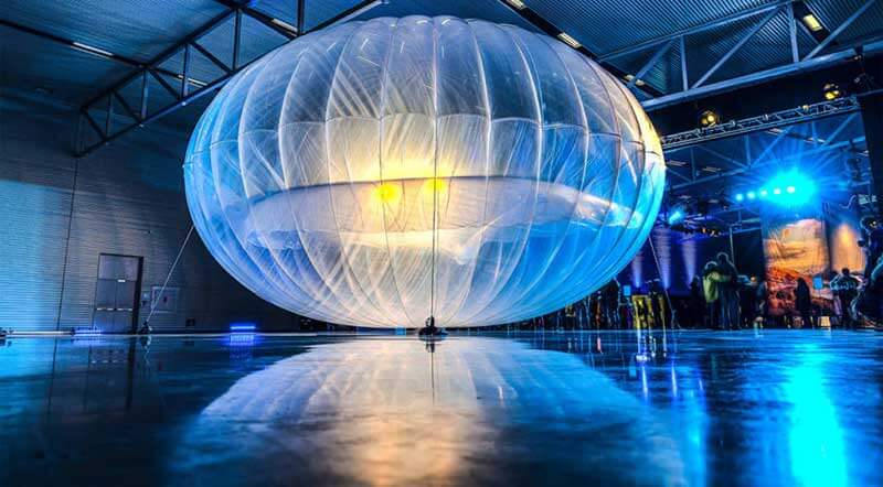 Project Loon balloon in a large, dark hall, with people standing in the background