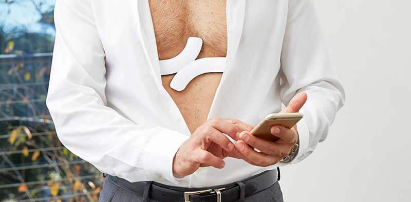 White QardioCore device on man’s chest peaking through his unbuttoned white shirt