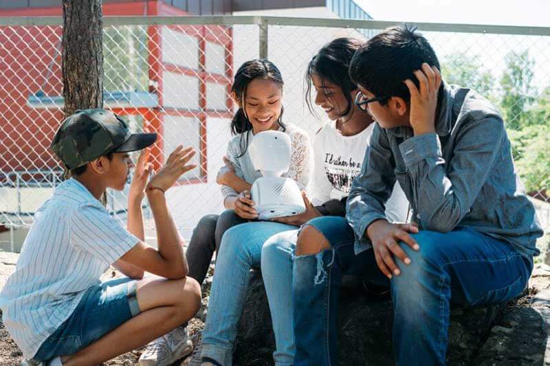 Four kids sitting and playing with a white robot