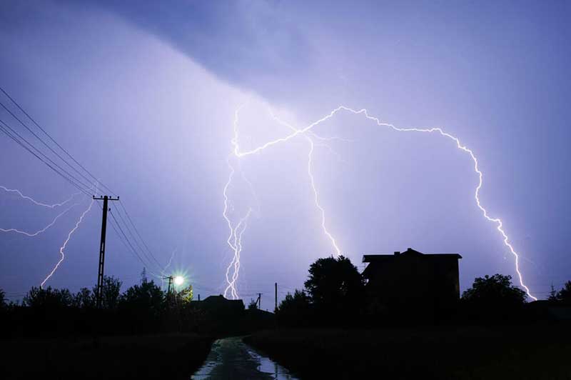 Several lightning bolts striking in proximity to power lines and houses