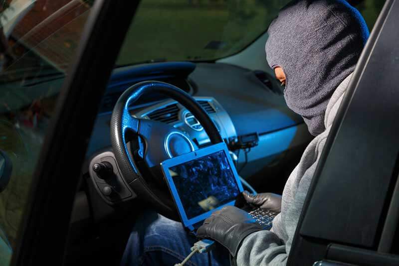Hacker sitting in a car and holding a laptop on his lap