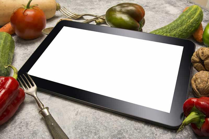 A tablet on a countertop, surrounded by vegetables and nuts