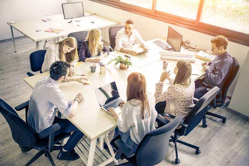 Bright office with large table surrounded by young professionals with laptops