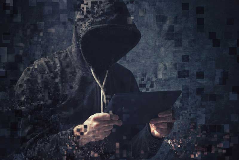 Man in a hoodie standing and holding a tablet with his face covered