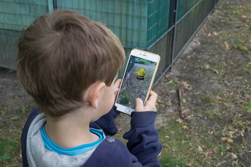 Child holding a smartphone and playing Pokemon Go outside