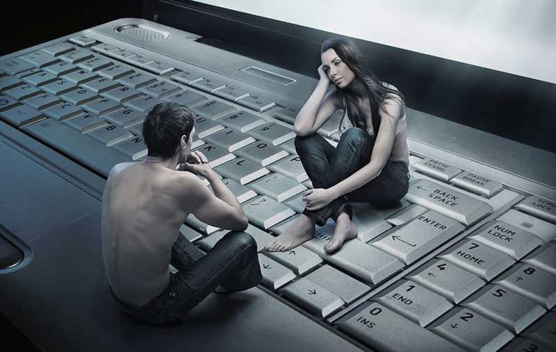 A man and a woman sitting on a laptop keyboard and looking at each other 