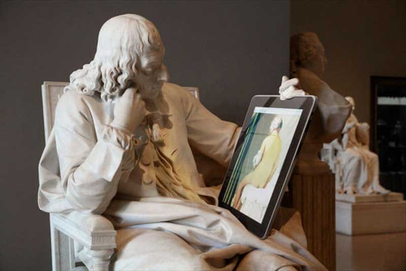 A sculpture of a man sitting down and it’s holding a tablet-like device