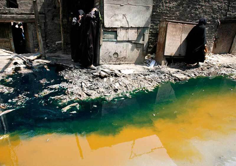 People standing next to a devastated building and polluted green-yellow water 