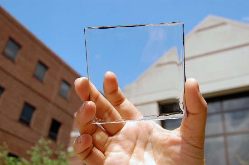 Close-up of a hand holding a transparent square-shaped piece of glass towards the sky