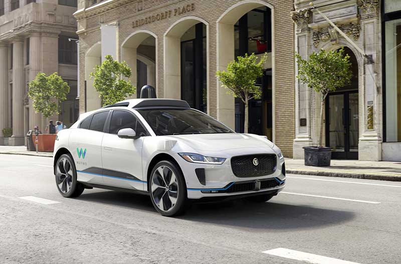 White self-driving car on a road next to old buildings 