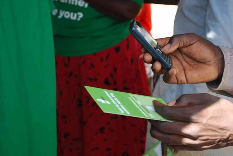 A person holding a green flyer in their left hand and a mobile phone in the right