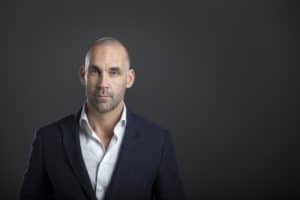 Man in a dark suit and a white shirt against a dark background (Richard van Hooijdonk)